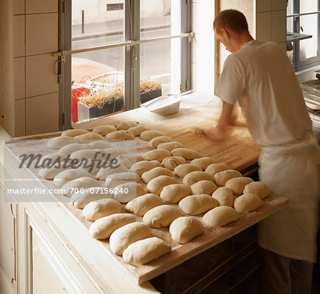 Male baker shaping baguette bread dough by hand in bakery, Le Boulanger des Invalides, Paris, France