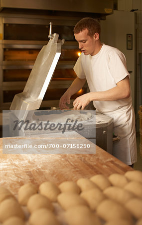 Male baker taking bread dough out of machine in bakery, Le Boulanger des Invalides, Paris, France