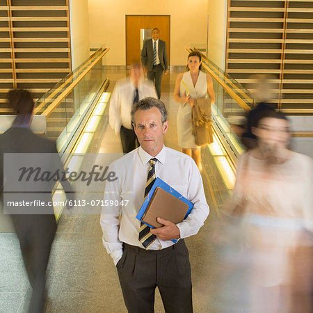 Businessman standing in busy office corridor