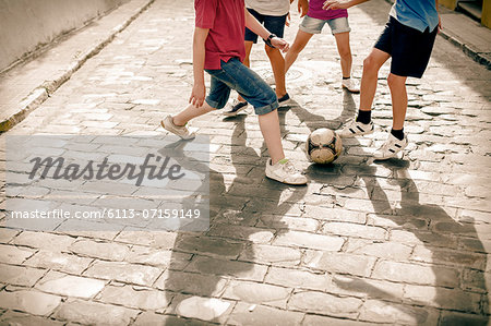 Children playing with soccer ball on cobblestone street