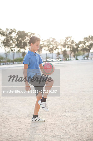 Boy kneeing soccer ball in sand