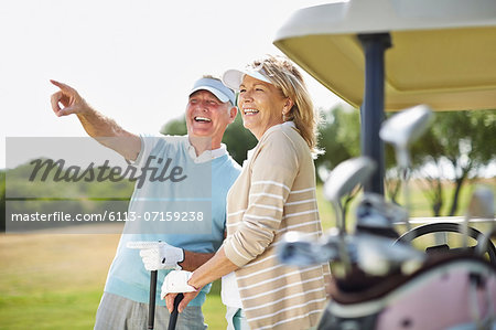 Senior couple standing next to golf cart