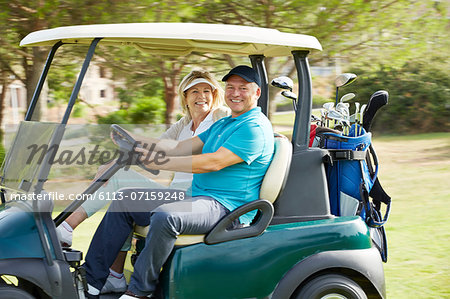 Senior couple driving golf cart on course