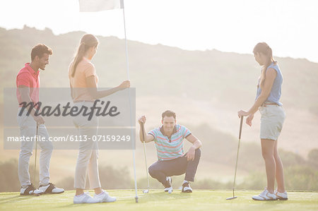 Friends watching man prepare to putt on golf course