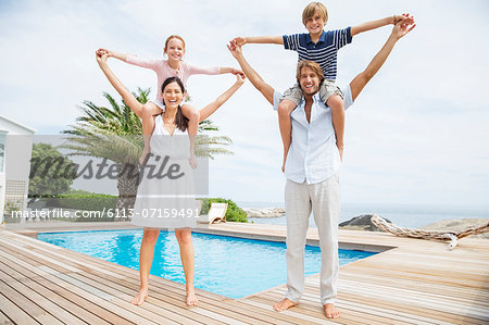 Parents carrying children on shoulders at luxury poolside
