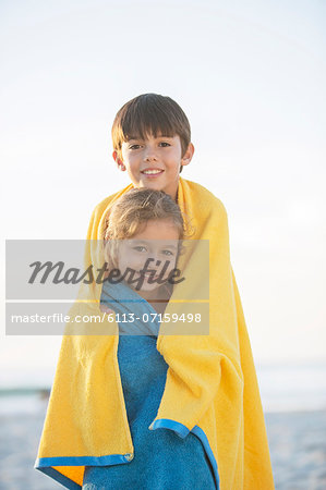 Brother and sister wrapped in towels on beach