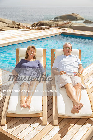Senior couple laying on lounge chairs at poolside