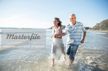 Older couple playing in waves on beach