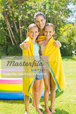 Mother wrapping daughters in towel in backyard