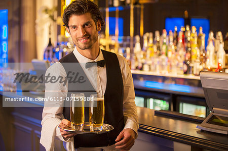 Portrait of well dressed bartender carrying beers on tray