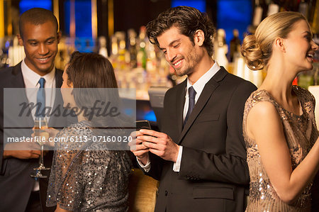 Well dressed man looking down at cell phone and smiling in luxury bar