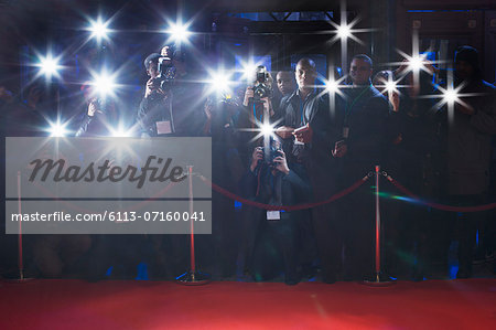 Paparazzi using flash photography behind rope on red carpet