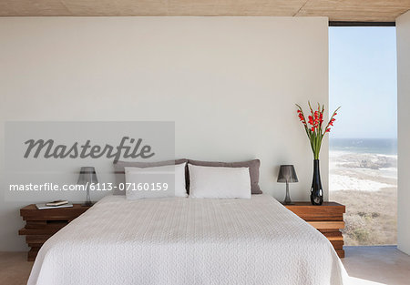 Vase of flowers next to bed in bedroom with ocean view