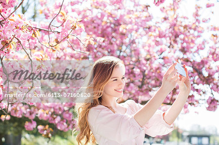 Woman taking self-portrait under tree with pink blossoms