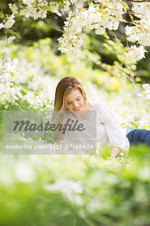 Woman reading book in grass under tree with white blossoms