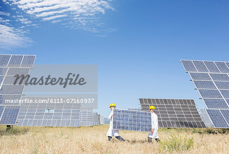 Scientists carrying solar panel in rural landscape