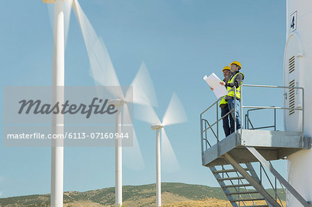 Workers standing on wind turbine in rural landscape