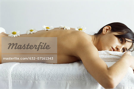 Woman lying on massage table, flowers lined up on her back