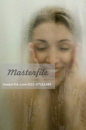 Woman behind wet glass, smiling, touching face