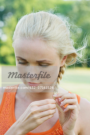 Young woman braiding hair, looking down in thought