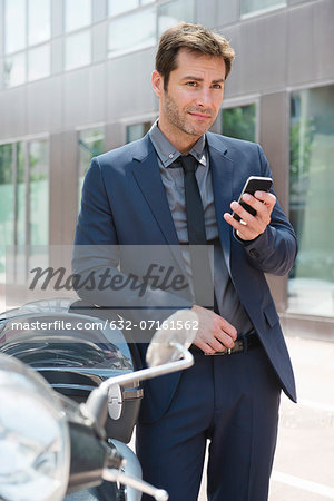 Businessman using smartphone in city, leaning against motor scooters Businessman using smartphone in city, leaning against motor scooters