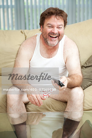 Unemployed man laughing and watching a funny show on television.