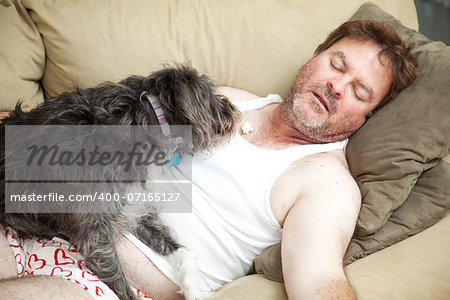 Unemployed man passed out on the couch in his underwear.  His dog is eating popcorn from his chest.