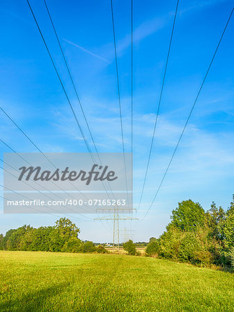 Power cable and power pole on a green meadow under a blue sky with white clouds