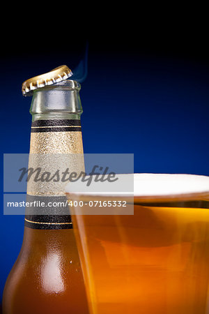 A cap is flying away from a beer bottle and a full glass.