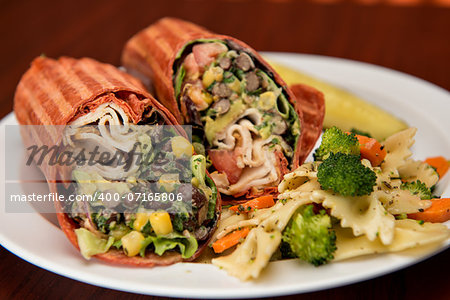 Southwest chicken wrap sliced in half on a white paper plate with a side of pasta salad.