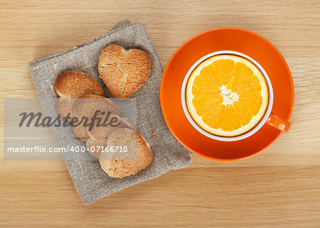 Cup with orange and heart shaped cookies on wooden table. View from above