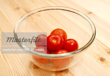 Fresh red tomatoes in a glass bowl, on a wooden table