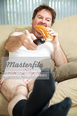 Unemployed man sitting on the couch in his underwear, watching TV and eating a sandwich.