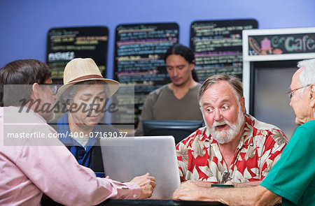 Four serious mature men in cafe with laptop