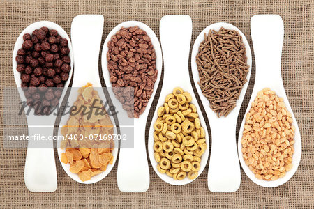 Breakfast cereal selection in white porcelain scoops over hessian background.