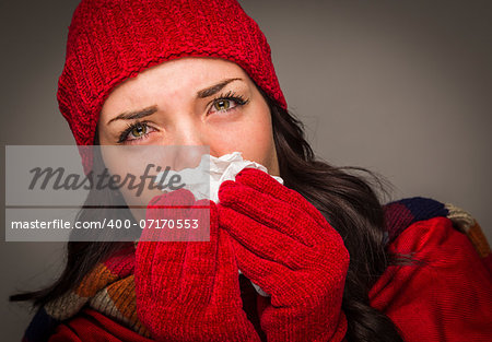 Sick Mixed Race Woman Wearing Winter Hat and Gloves Blowing Her Sore Nose with a Tissue.