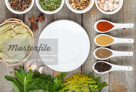 Colorful herbs and spices selection. Aromatic ingredients on wood table with empty plate for copyspace