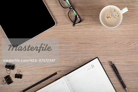 Tablet, notepad, glasses and coffee cup on office wooden table