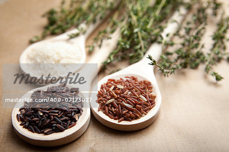 red and white rice in a wooden spoons, herbs thyme, on paper background