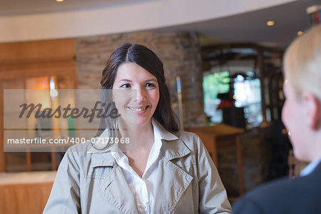 Smiling attractive young female guest in a hotel lobby talking to the receptionist as she checks in on her arrival