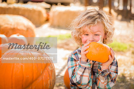 Adorable Little Boy Sitting and Holding His Pumpkin in a Rustic Ranch Setting at the Pumpkin Patch.