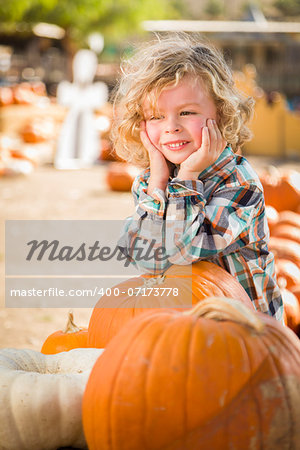 Adorable Little Boy Smiles While Leaning on a Pumpkin at a Pumpkin Patch in a Rustic Setting.