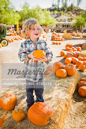 Adorable Little Boy Sitting and Holding His Pumpkin in a Rustic Ranch Setting at the Pumpkin Patch.