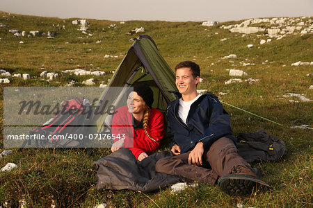 A young couple is watching the sunset while camping in the mountains