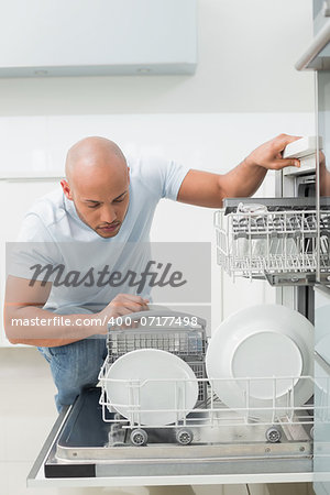 Serious young man using dish washer in the kitchen at home