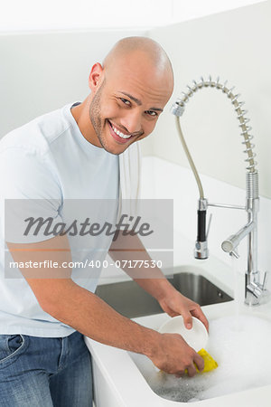 Portrait of a smiling young man doing the dishes at kitchen sink in the house