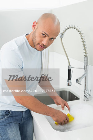 Portrait of a young man doing the dishes at kitchen sink in the house