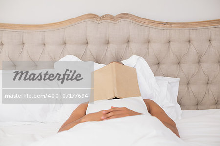 Relaxed young man with book over face lying in bed at home