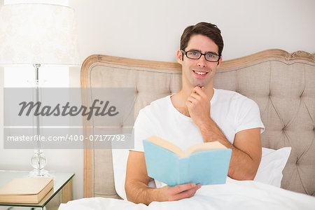 Portrait of a relaxed young man reading book in bed at house