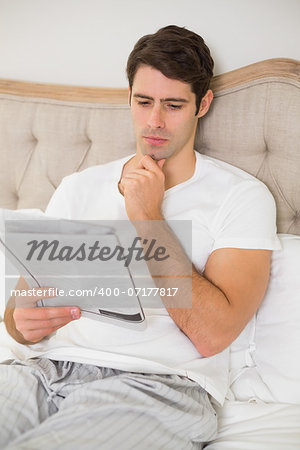 Casual young man reading newspaper in bed at home